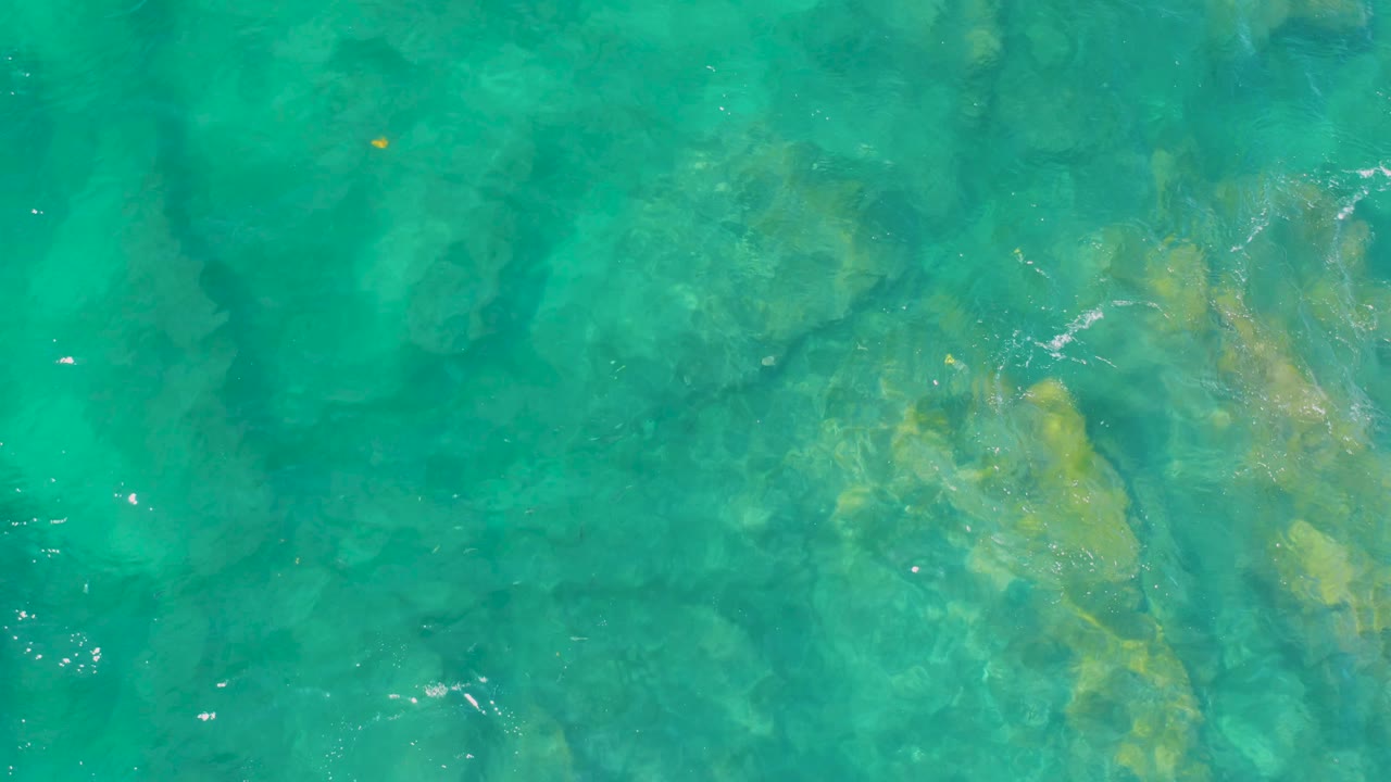 Clear coastal water reveals beige rock forms below the surface at Shipwrecks Beach, Baja California Sur, with scattered sparkle points and no visible people.