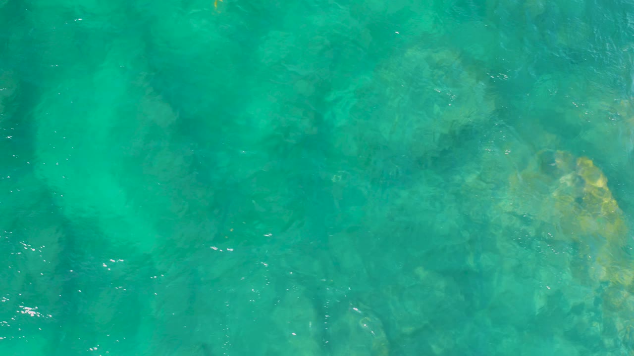 An overhead view shows green-blue water and darker seafloor shapes at Shipwrecks Beach, Baja California Sur, with no visible people.