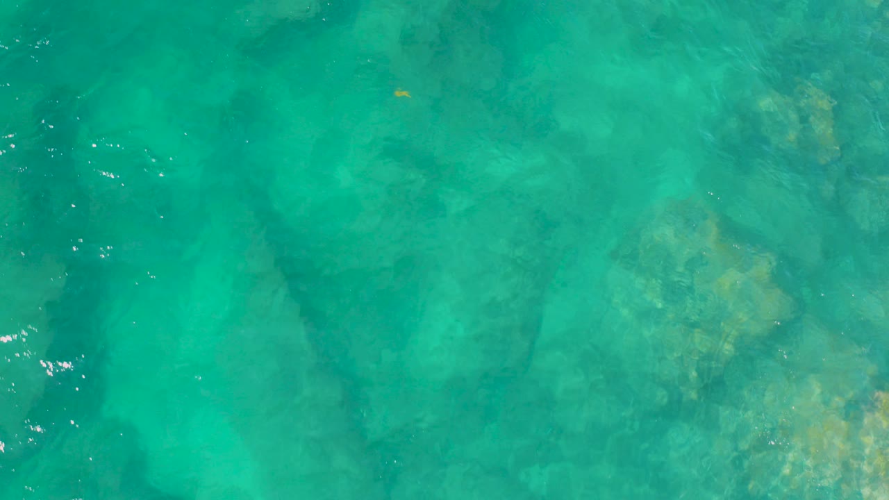 Top-down turquoise seawater with submerged rock shapes.