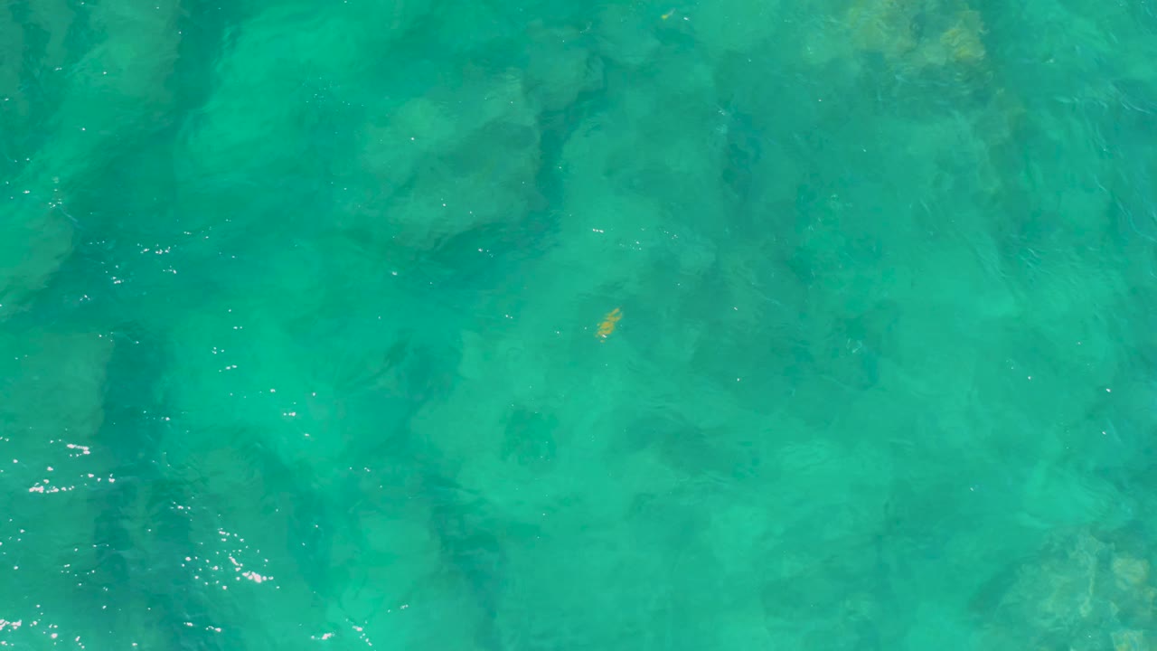 Clear teal water with submerged rocks and small highlights on the surface.