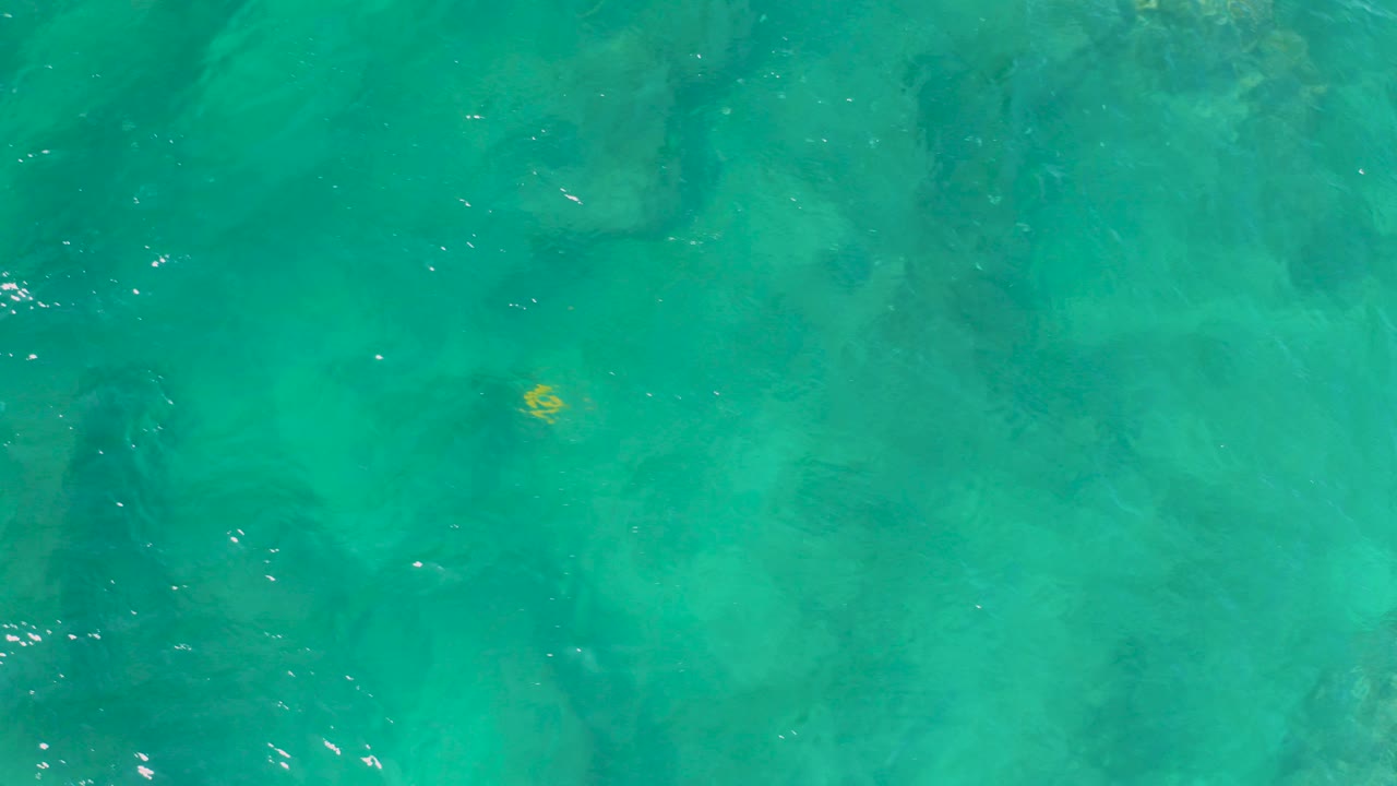 Top-down turquoise ocean water at Shipwrecks Beach, Baja California Sur, with darker submerged patches and no visible people.