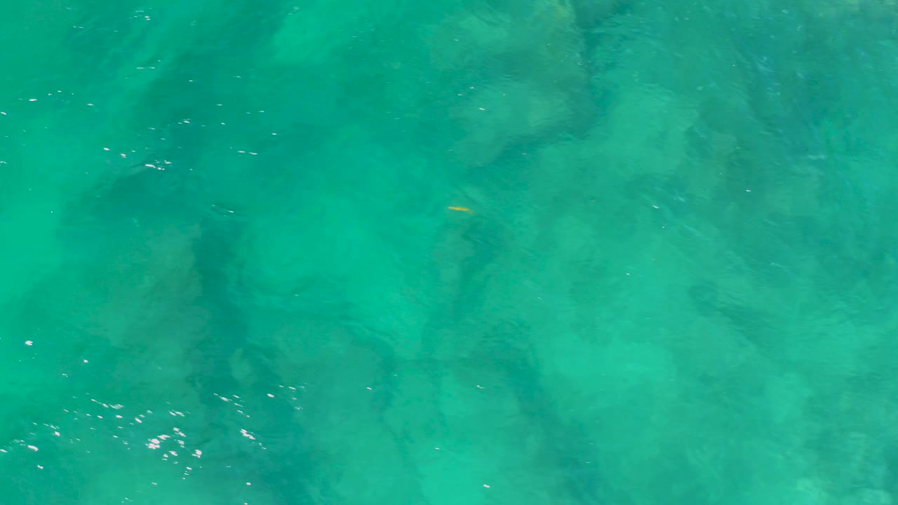 Top-down view of turquoise water at Shipwrecks Beach, Baja California Sur, with darker submerged rock or reef shapes and no visible people.