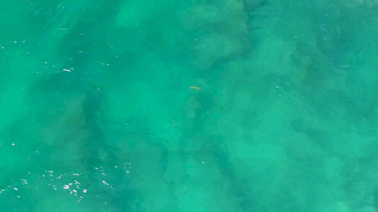 Clear green-blue water fills the frame at Shipwrecks Beach, with soft ripples crossing darker underwater forms and no visible people.