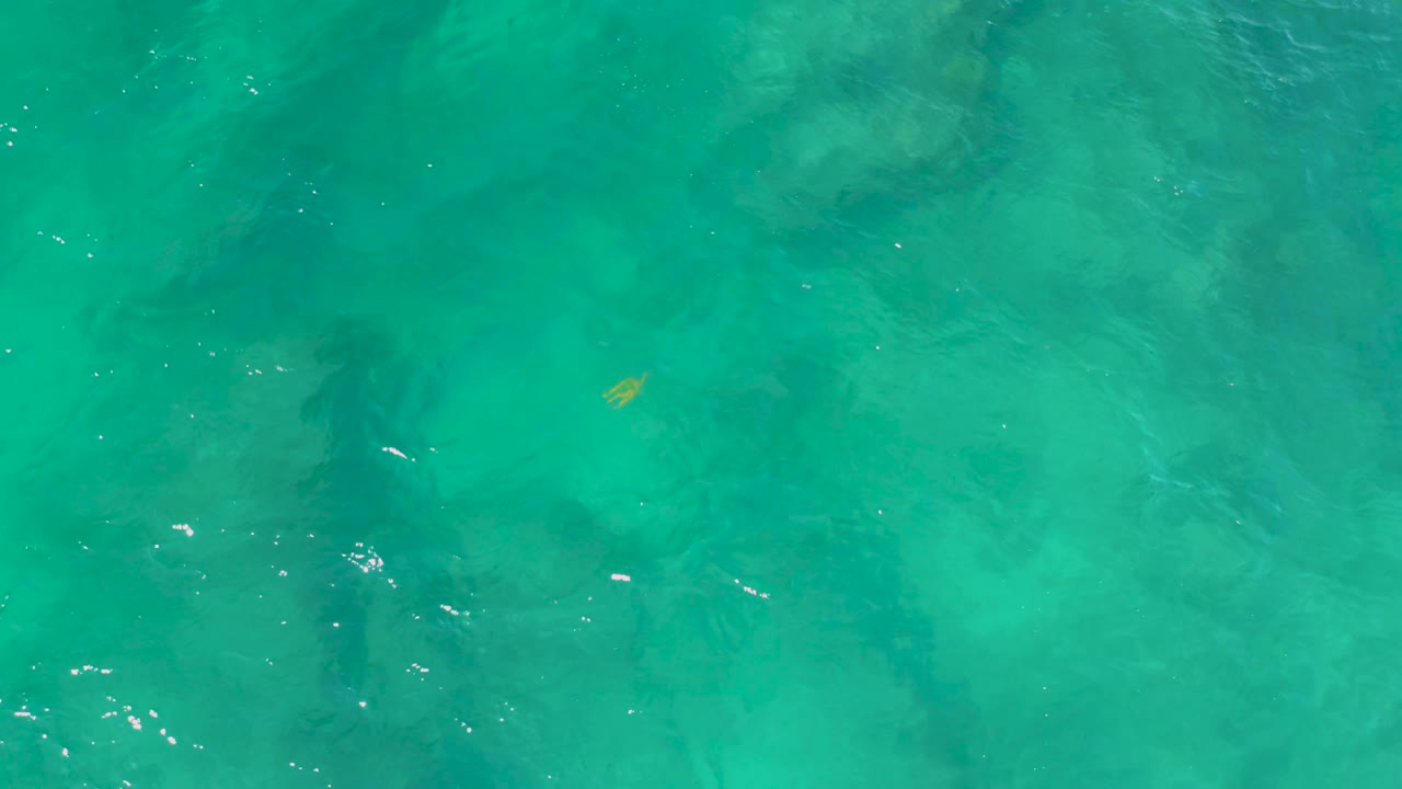Turquoise water at Shipwrecks Beach shows pale ripples crossing darker green forms beneath or reflected on the surface, with no visible people.