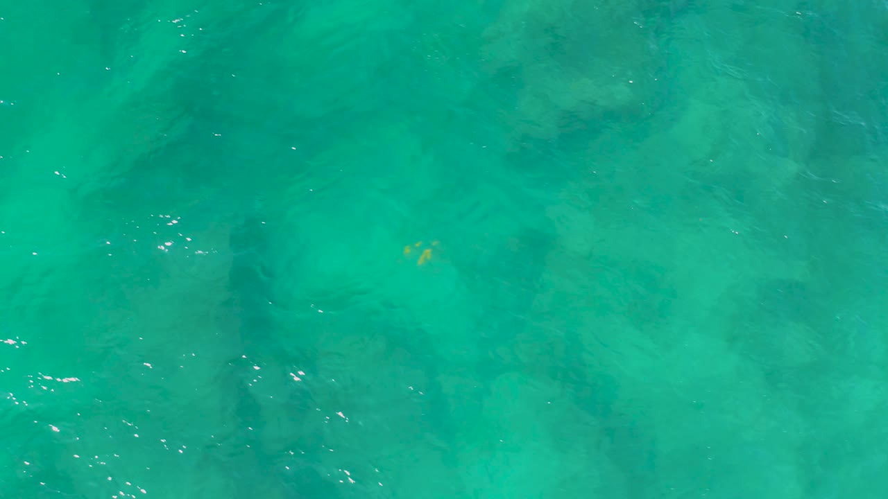 Teal-green Shipwrecks Beach water fills the overhead frame with darker vertical shadow areas and scattered white highlights, with no visible people.