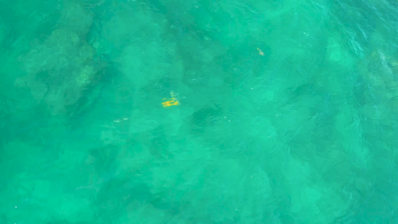 Shallow turquoise water at Shipwrecks Beach in Baja California Sur, Mexico, with darker rock shapes below and a yellow fish detail on the left, no visible people.