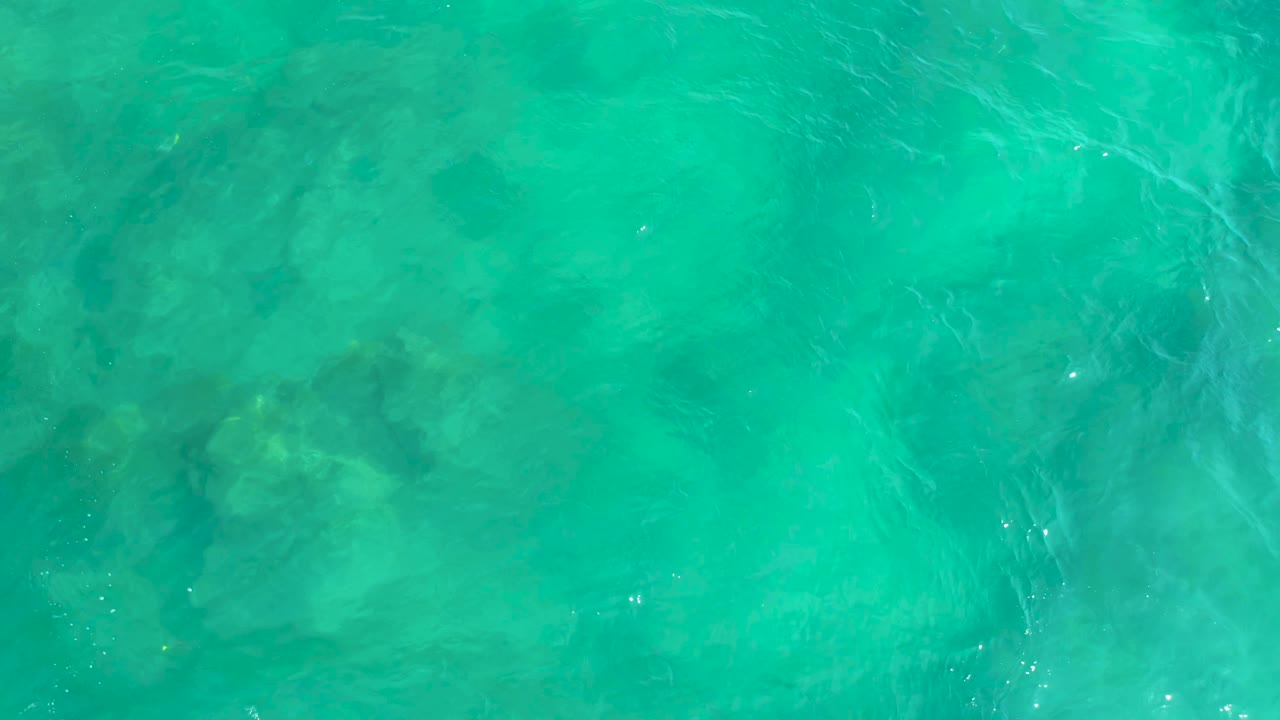 Overhead view of turquoise water at Shipwrecks Beach, Baja California Sur, with faint submerged dark shapes near the left side and no visible people.