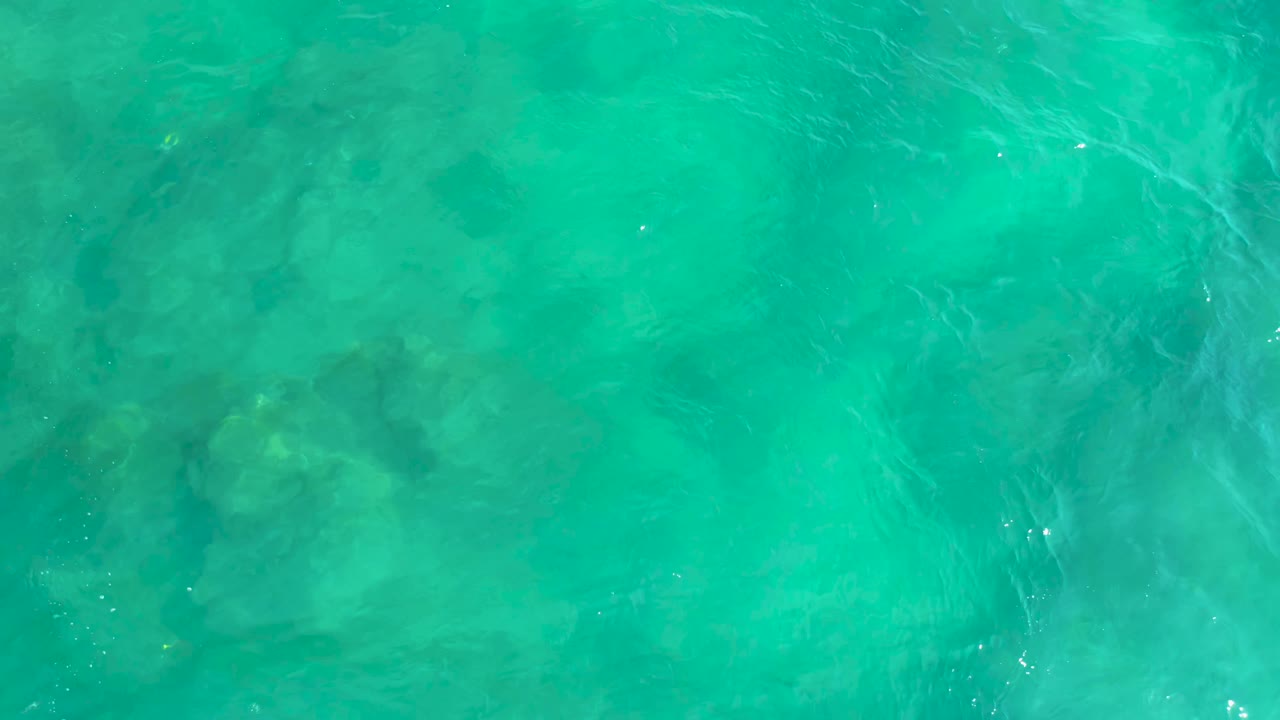 Blue-green ocean water fills the frame at Shipwrecks Beach, with darker submerged forms visible through the ripples and no visible people.