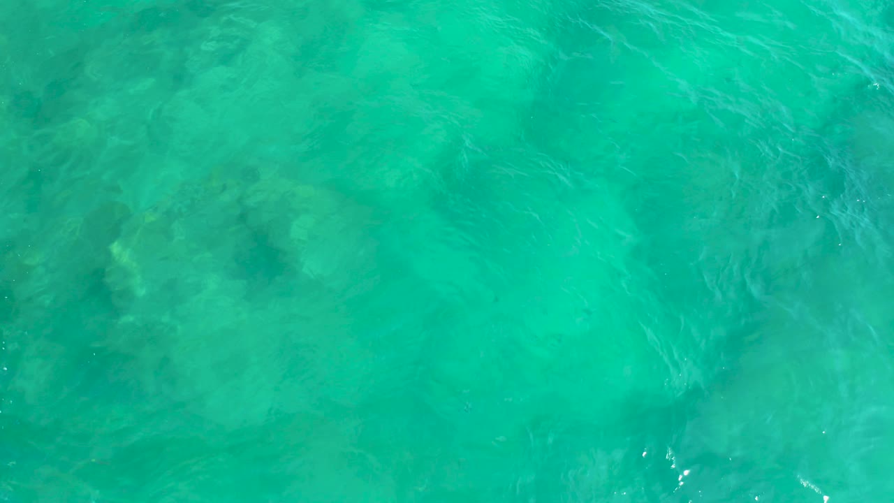 Overhead water at Shipwrecks Beach in Baja California Sur, Mexico, with turquoise color, darker underwater shapes, and brighter white ripple streaks toward the right, no visible people.