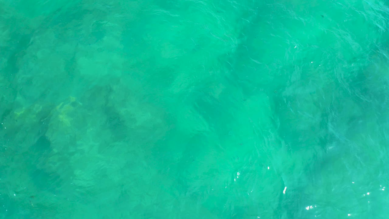 Turquoise ocean water with faint submerged rocks and surface ripples.