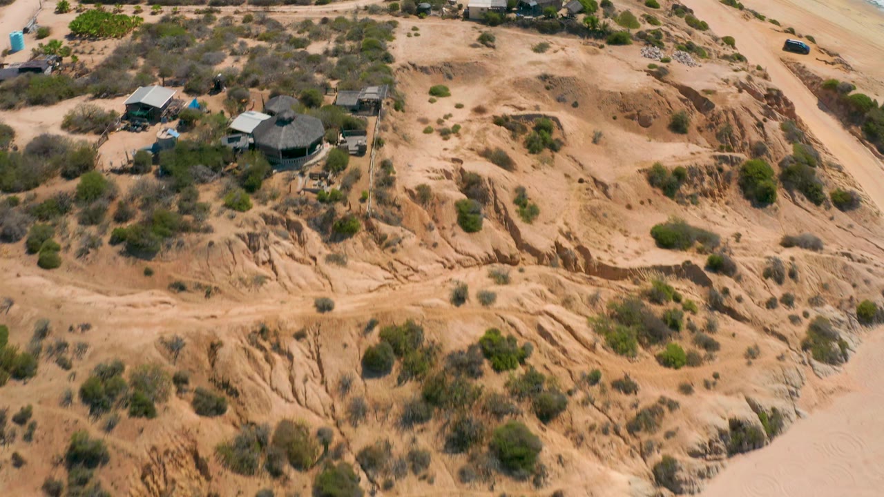 Overhead view of scrub-covered coastal land with a round-roof building and sandy gullies.