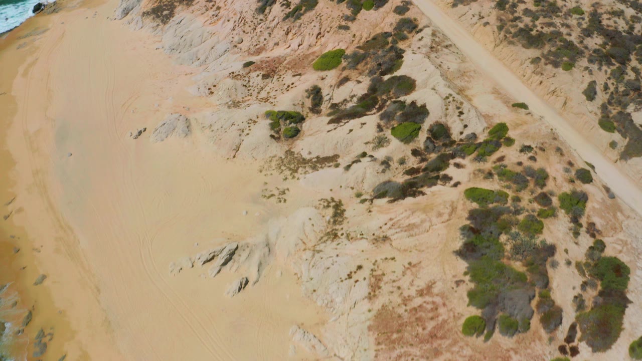Overhead sandy beach with rocks, scrub, and a diagonal track.