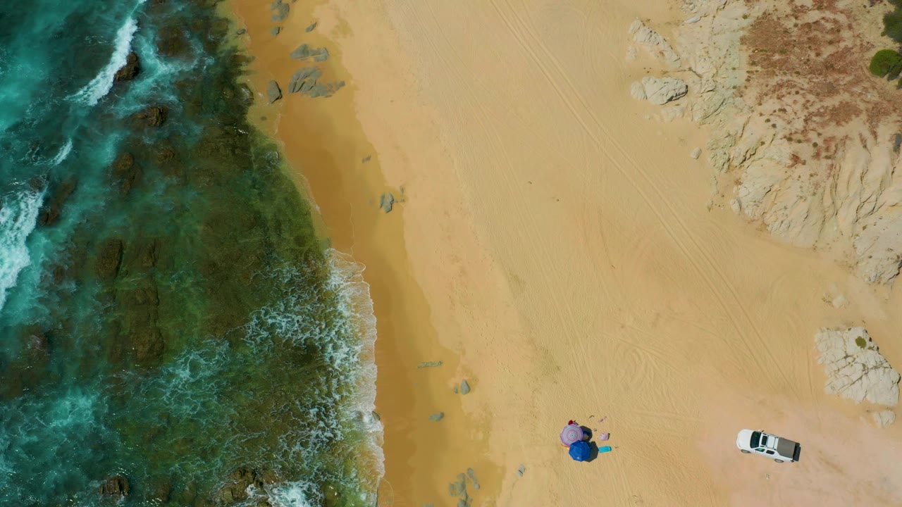 Drone view of surf and reef meeting a wide sandy beach.