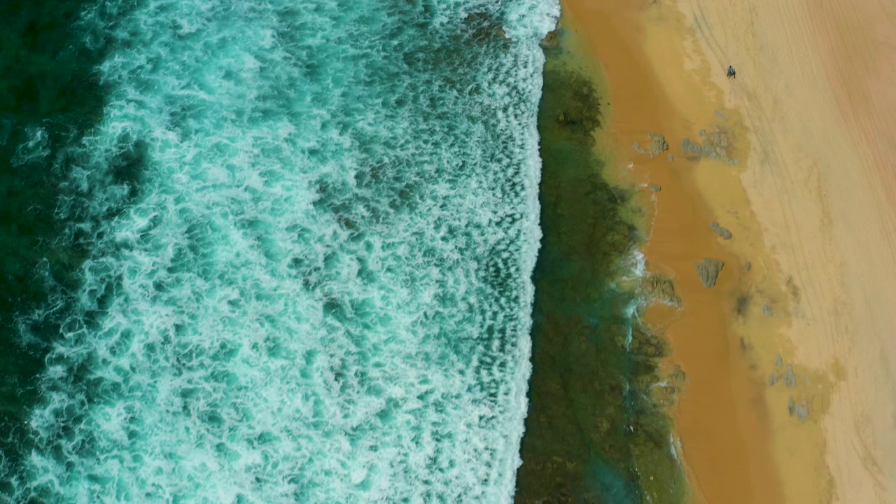 Green surf and whitewater dominate the upper and left areas, while a strip of wet reef and golden sand forms the beach edge at Shipwrecks Beach, Baja California Sur.