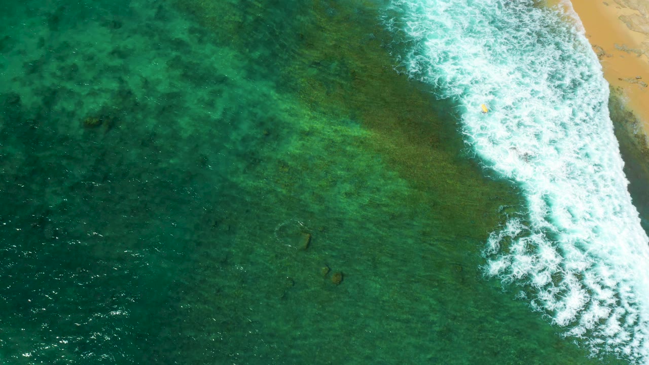 White foam spreads across green-blue shallow water near sand.