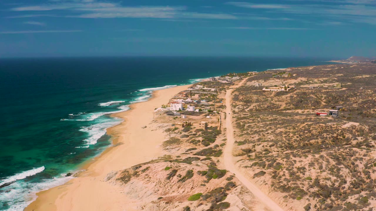 High coastal view of waves breaking beside a sandy beach and scrubland.