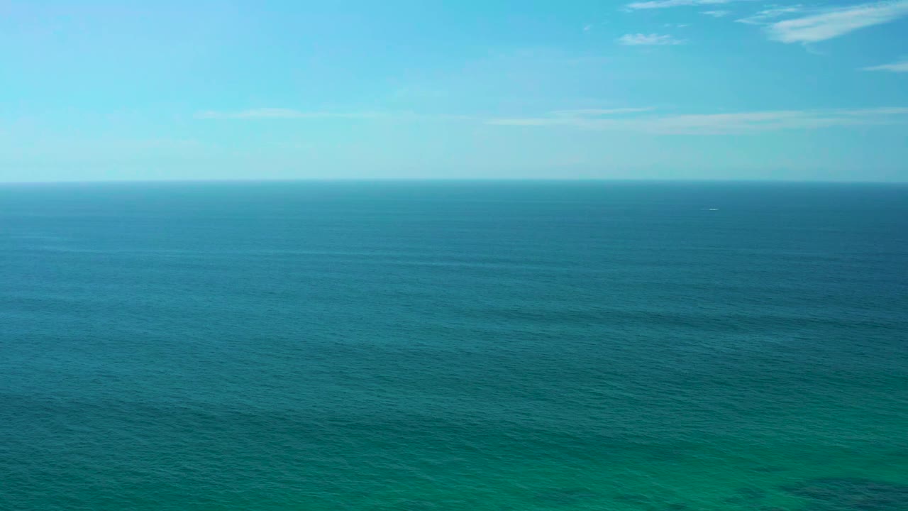 Open ocean surface beneath pale blue sky.