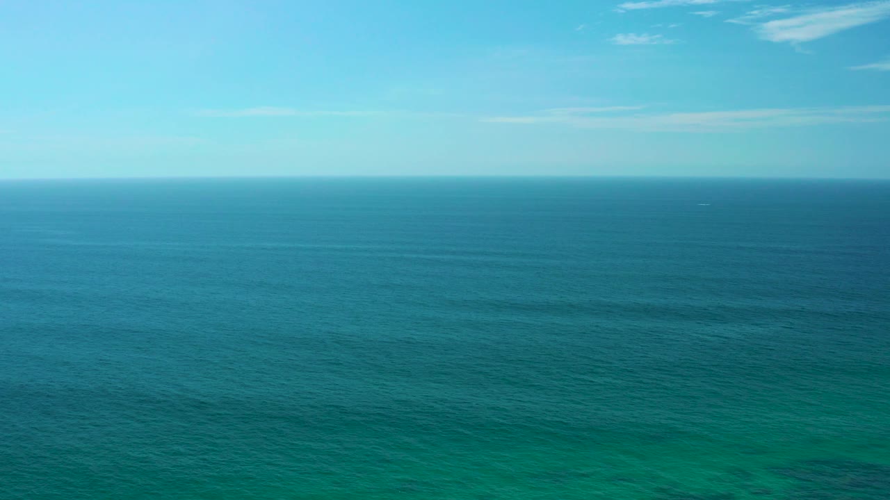 Blue sea and sky meet at a distant horizon near Shipwrecks Beach, Baja California Sur, with small cloud streaks overhead and no visible people.