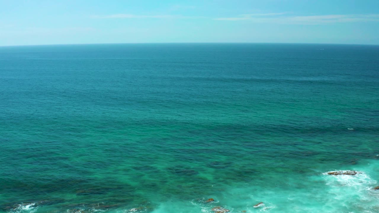 At 0:02, the frame shows Shipwrecks Beach water stretching to the horizon, with darker reef shapes below the surface, whitewater around rocks, and no visible people.