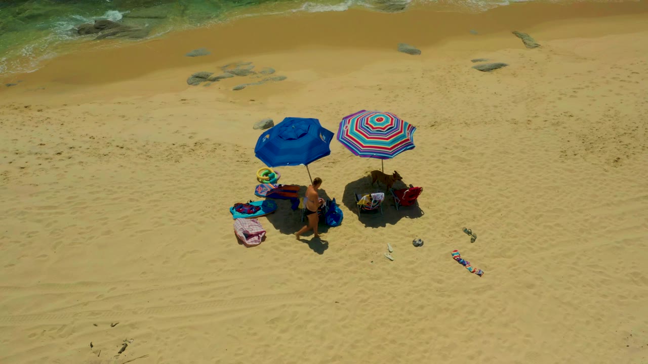 Two adults remain near umbrellas and beach gear on a mostly empty sandy beach.