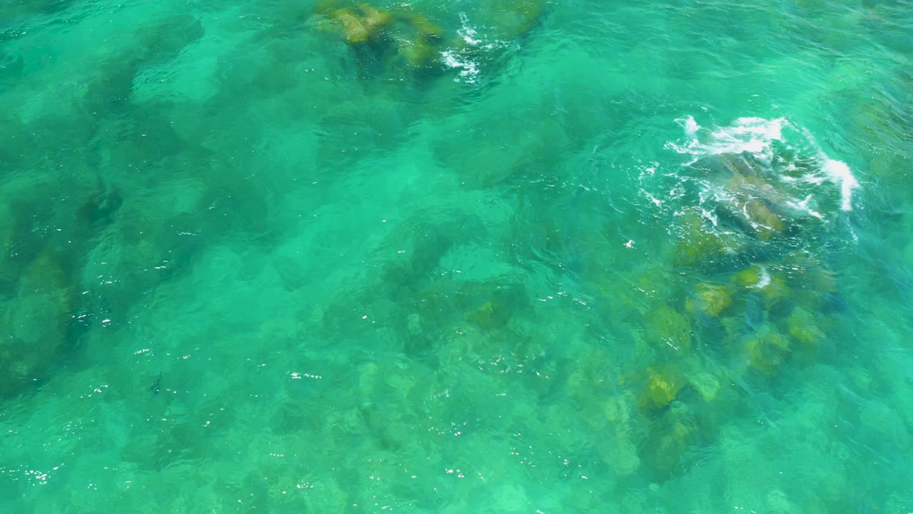 Overhead view of turquoise water at Shipwrecks Beach with submerged rocks near the upper center and lower middle, no visible people.