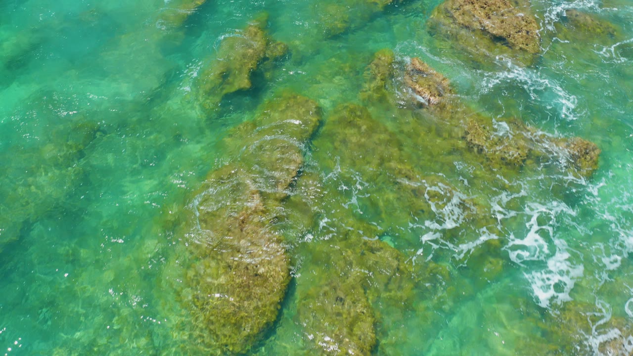 Overhead view at Shipwrecks Beach in Baja California Sur showing clear turquoise water over broad submerged rocks, with no visible people.