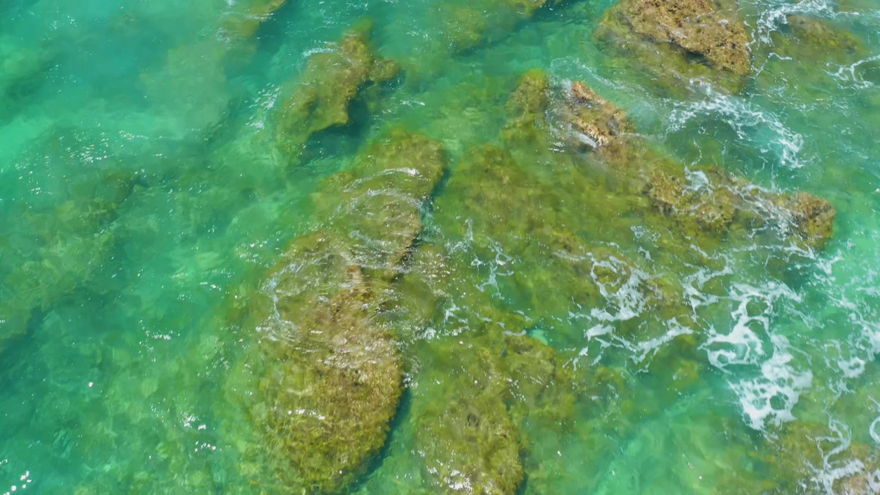 Clear green-blue water surrounds several tan rocks.