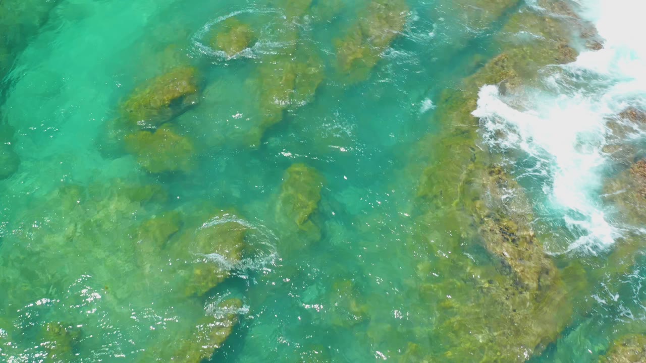 Green-blue seawater moving around shallow brown rock formations.