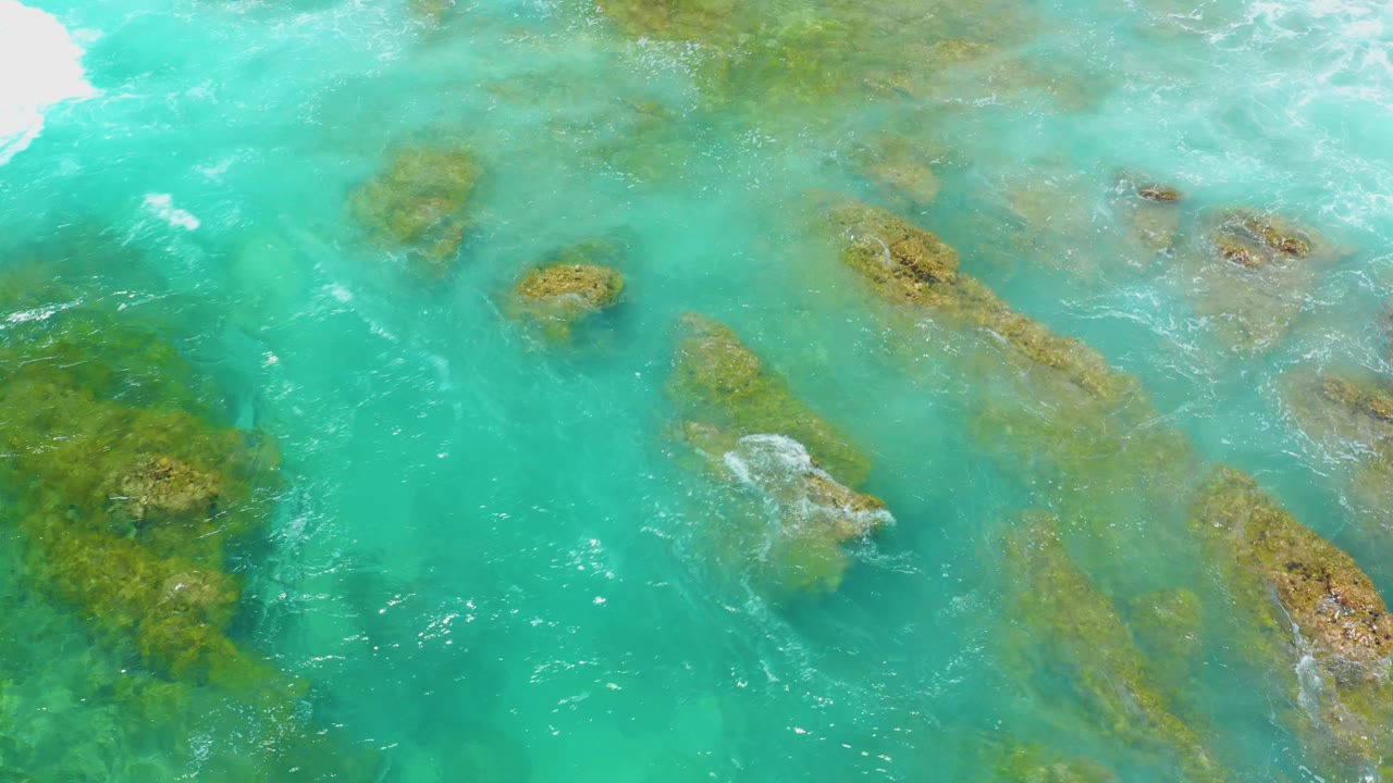 Overhead view of turquoise water at Shipwrecks Beach, Baja California Sur, with submerged brown-green reef patches and small white surf marks, no visible people.