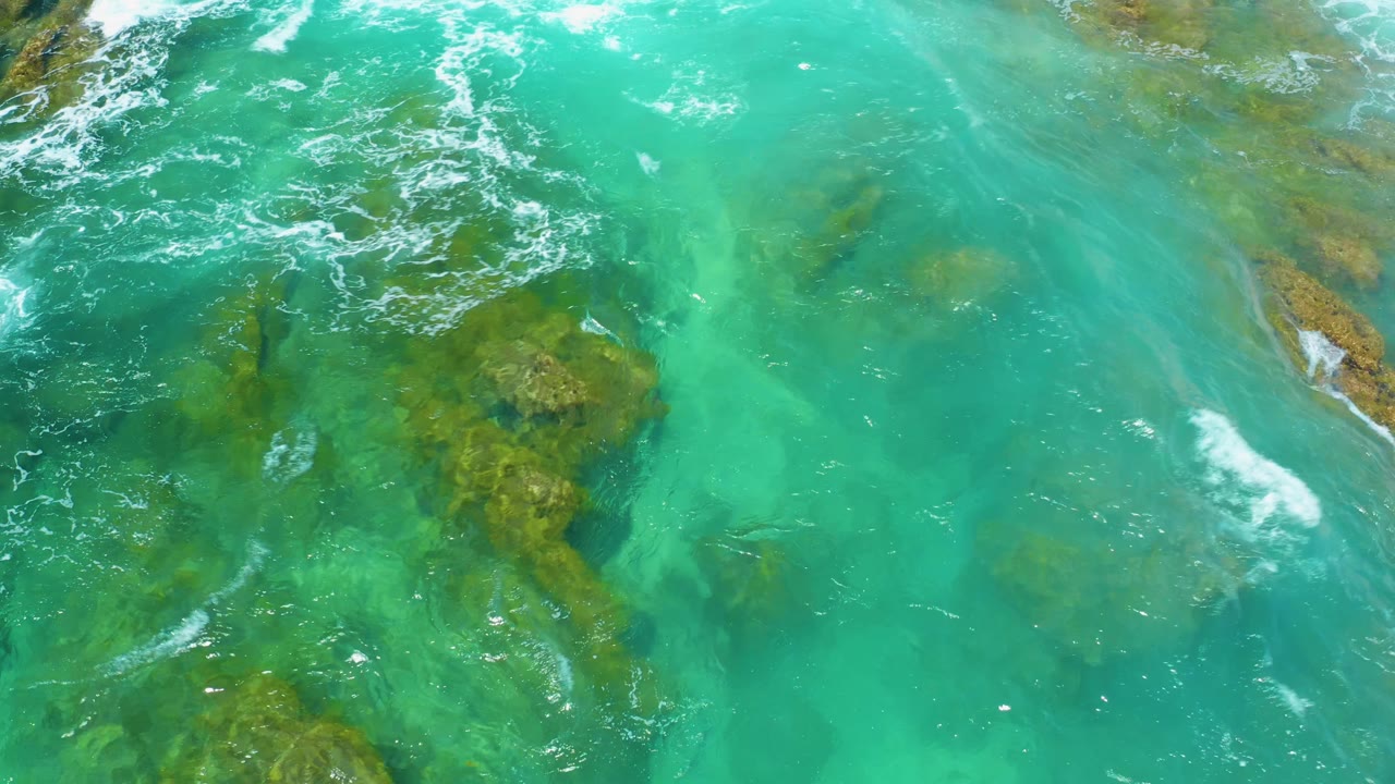 Clear green-blue water with reef patches and small foam streaks across the top.