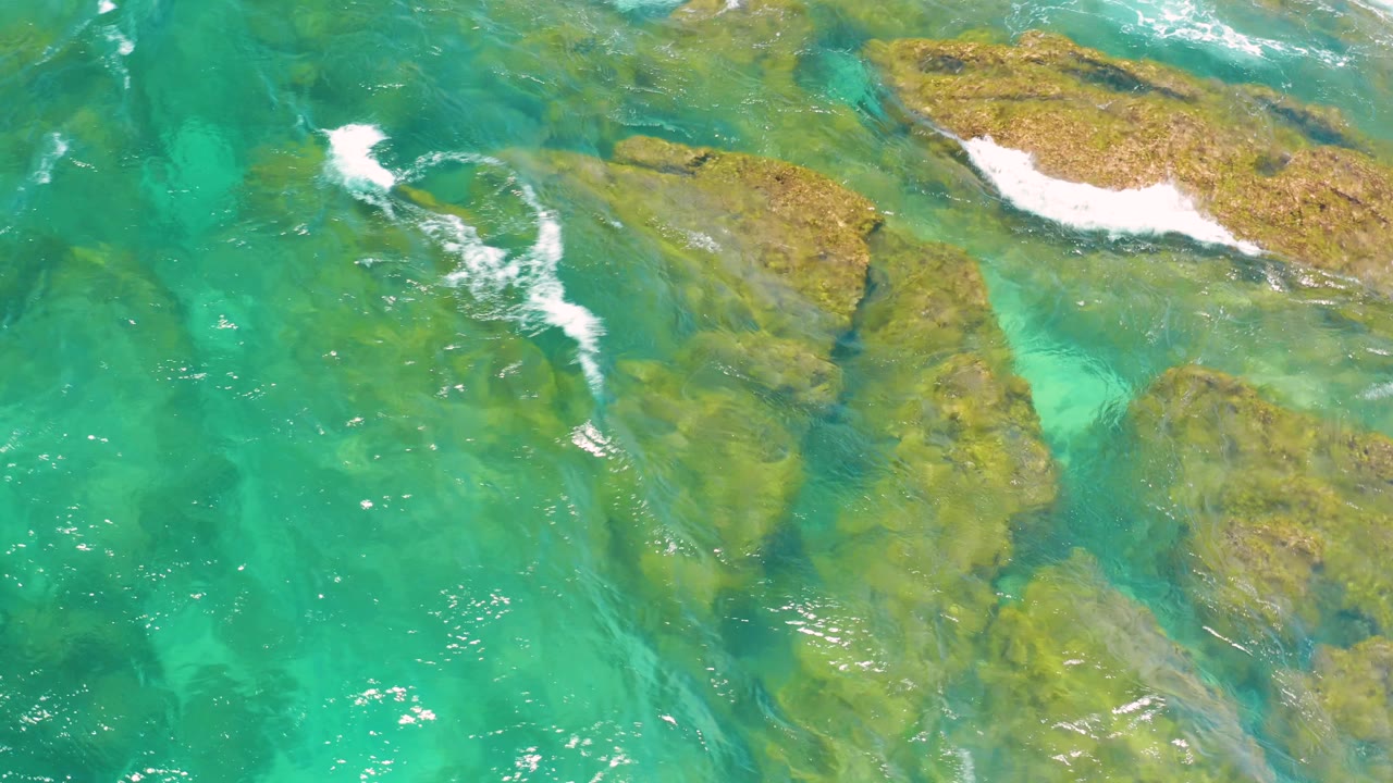 Foam trails stretch diagonally over green water and rock shelves at Shipwrecks Beach, with no visible people or structures.