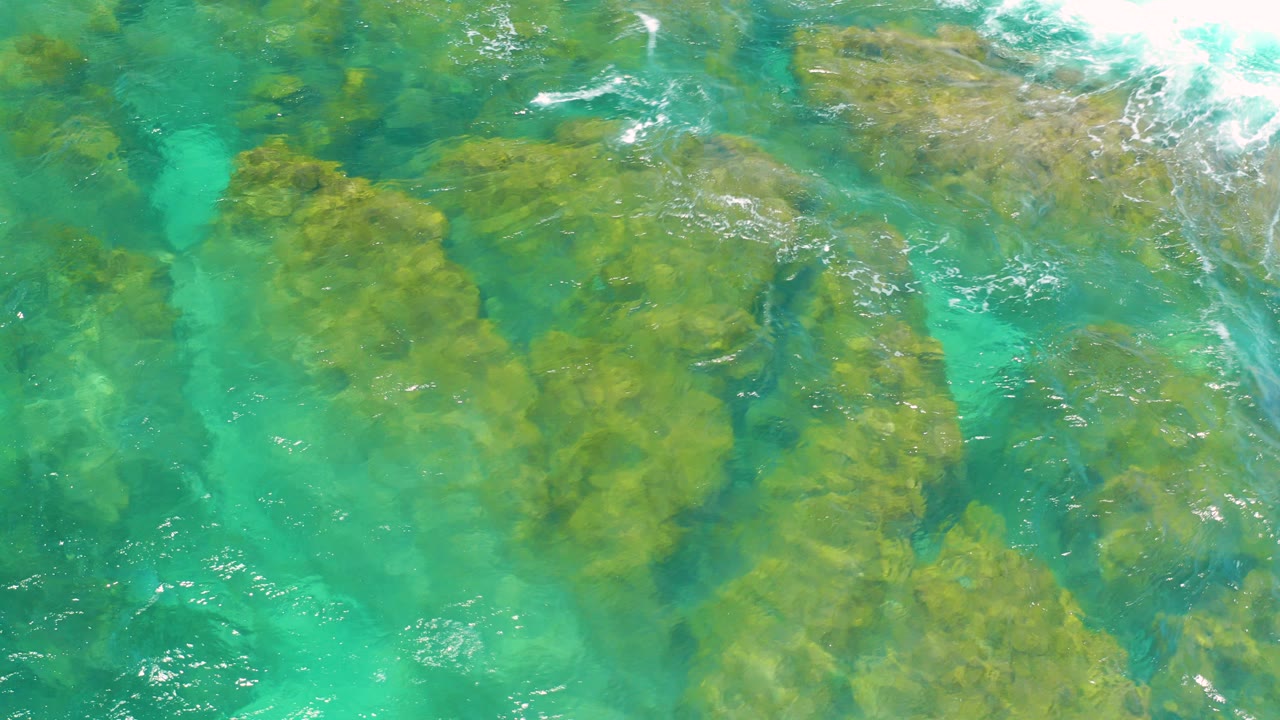 Overhead view of turquoise water covering tan submerged rocks at Shipwrecks Beach in Baja California Sur, with no visible people.