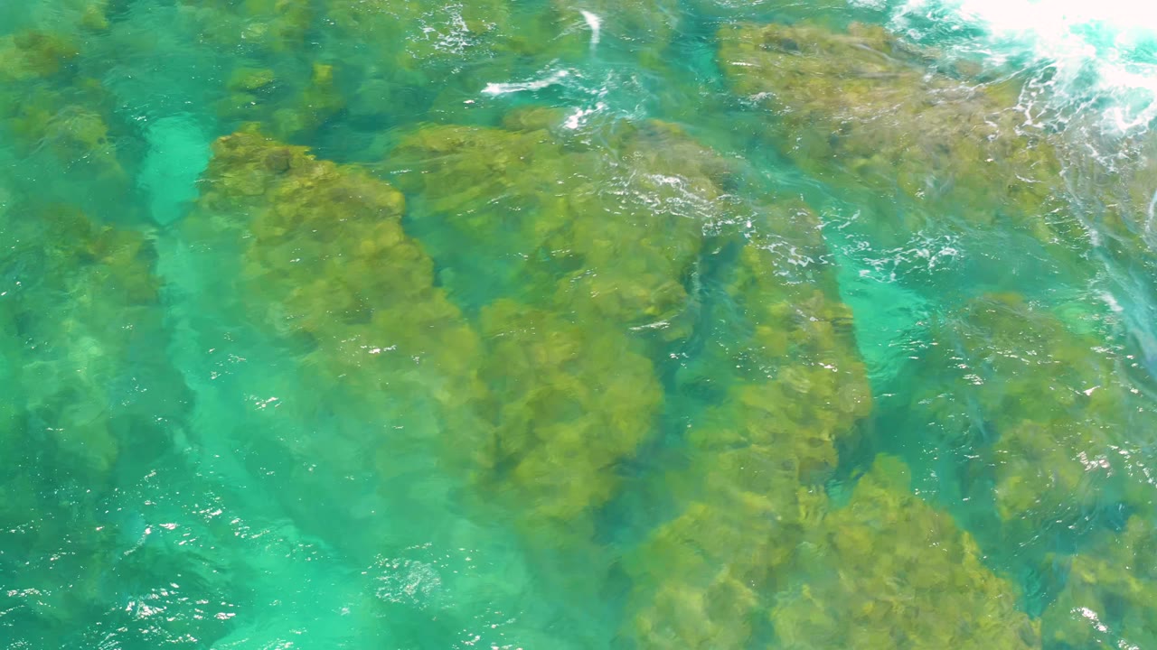 Blue-green sea water passes over clustered submerged rocks at Shipwrecks Beach, with small white ripples and no visible people.