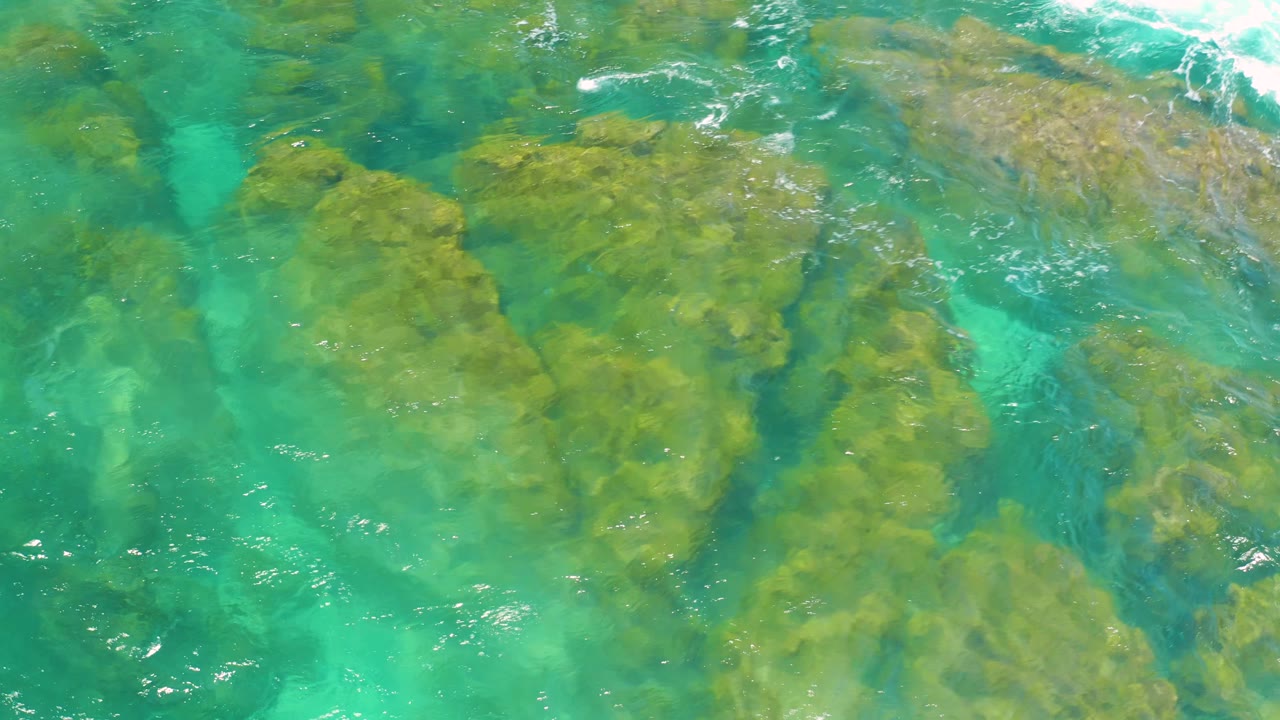 Clear turquoise water reveals rounded tan and brown rocks below the surface at Shipwrecks Beach in Baja California Sur, with no visible people.