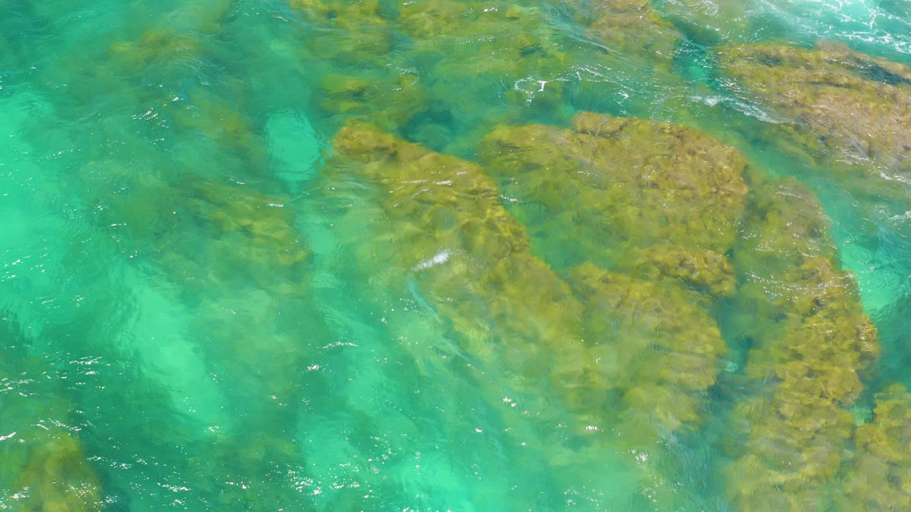 Turquoise water over submerged shoreline rocks.