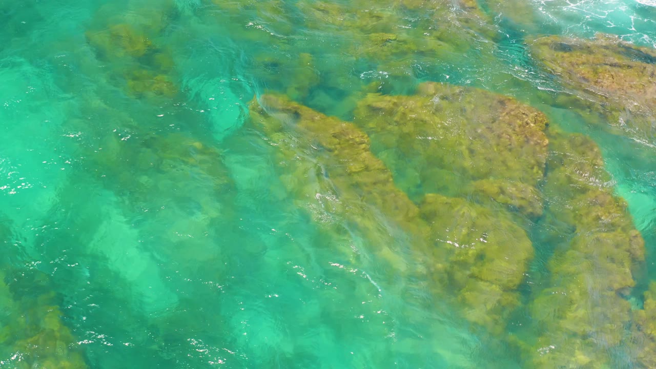 Top-down view of bright turquoise shallows over broad weathered rocks at Shipwrecks Beach in Baja California Sur, Mexico, with no visible people.