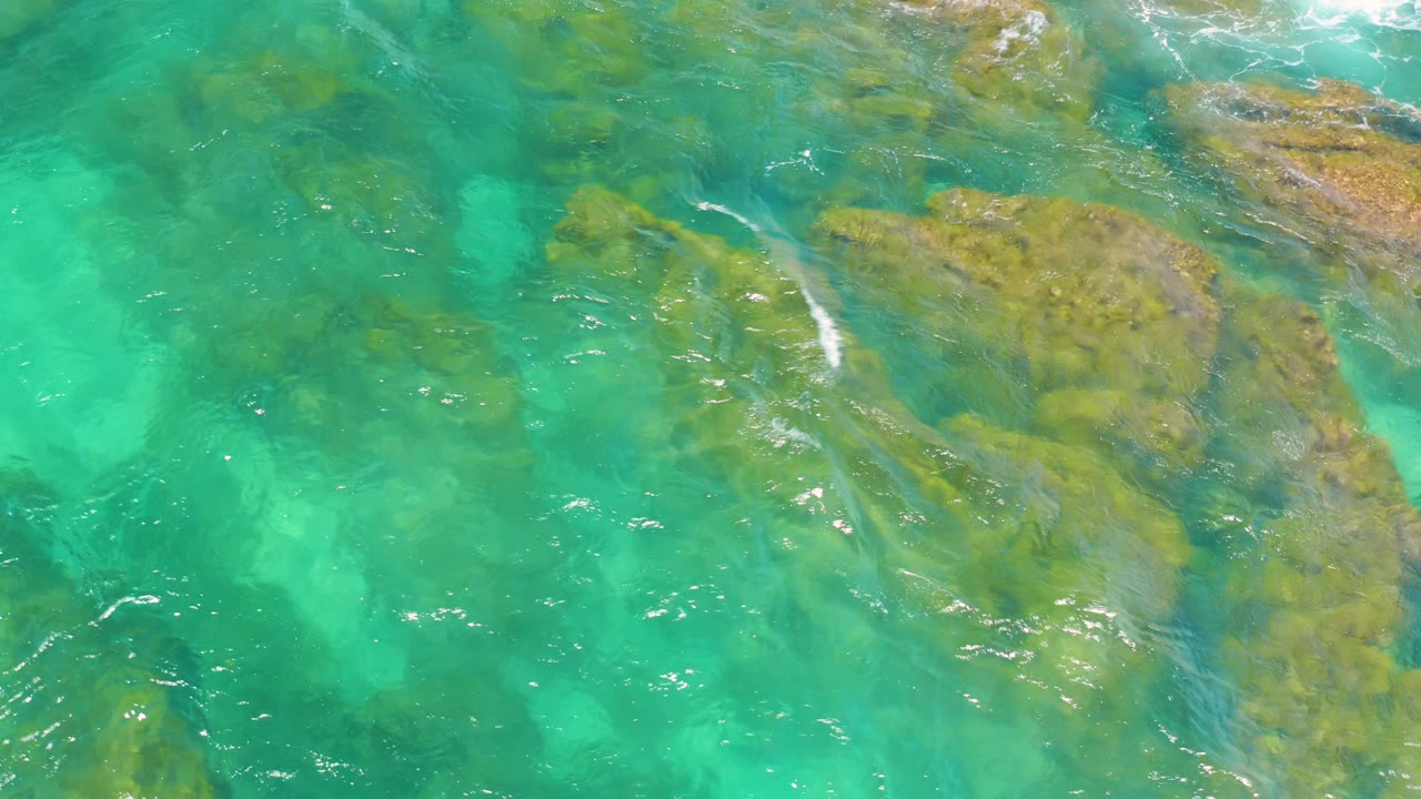 Clear turquoise water crosses diagonal yellow-brown rocks at Shipwrecks Beach, with a few thin white wave streaks and no visible people.