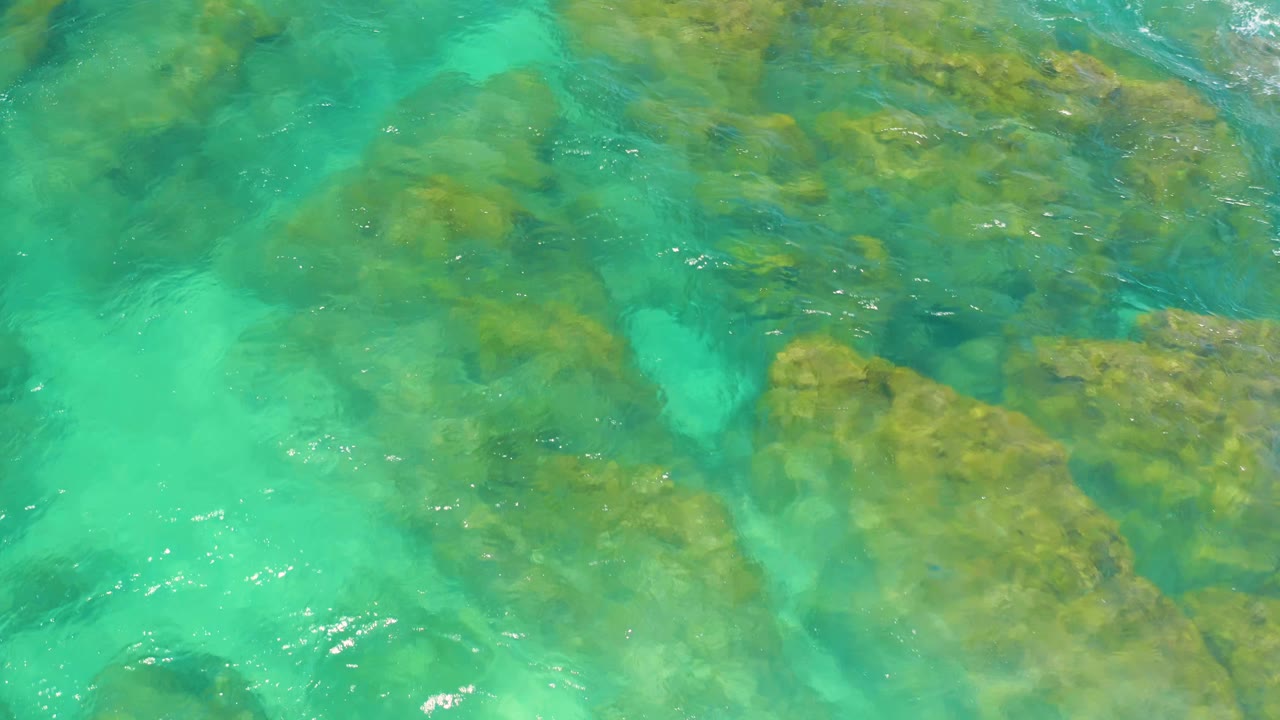 Green-blue shallow water flows around broad submerged rock shelves at Shipwrecks Beach, Baja California Sur, with no visible people.