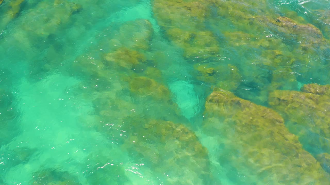Top-down coastal detail of turquoise water and brown rock patches under the surface at Shipwrecks Beach, Baja California Sur, with no visible people.