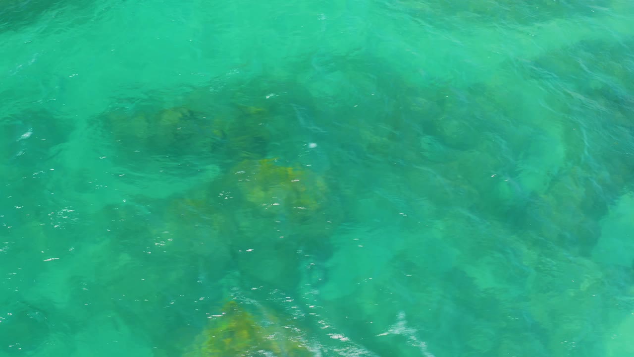 Clear green-blue water at Shipwrecks Beach shows shadowy rock forms beneath rippled surface light and no visible people.