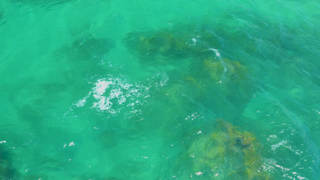 Turquoise ocean at Shipwrecks Beach fills the frame, with white foam near center left, rock patches beneath the surface, and no visible people.