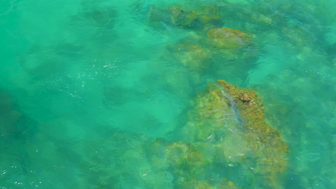 Overhead view of turquoise water over submerged rocks and sandy patches at Shipwrecks Beach, Baja California Sur, with no visible people.