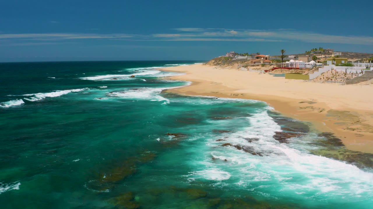Aerial coastline with white surf spreading over rocks and sand.