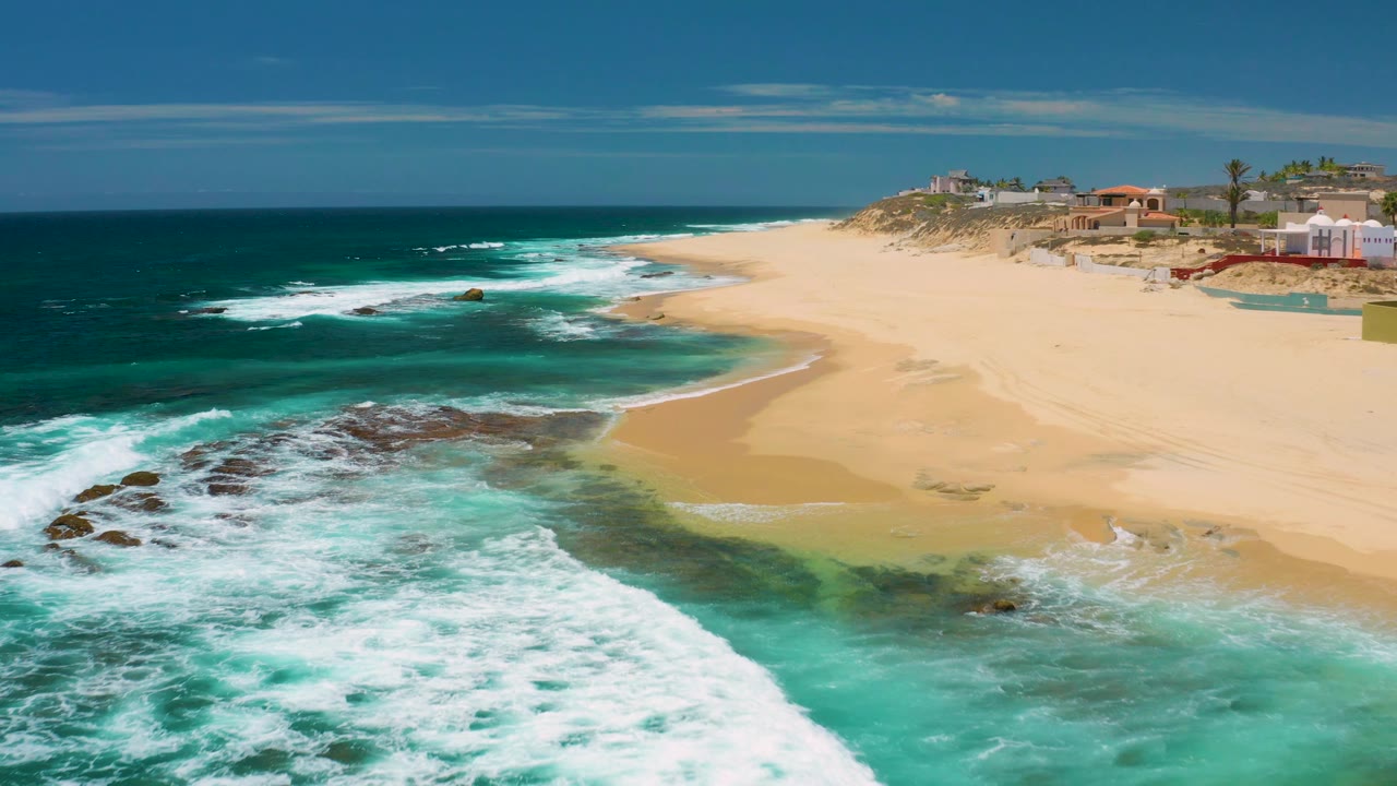 Rocky surf fills the foreground with an empty beach and coastal properties beyond.