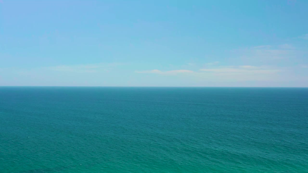 Aerial ocean view at Shipwrecks Beach with blue-green water filling most of the frame, a clean horizon line, light haze, and no visible people.