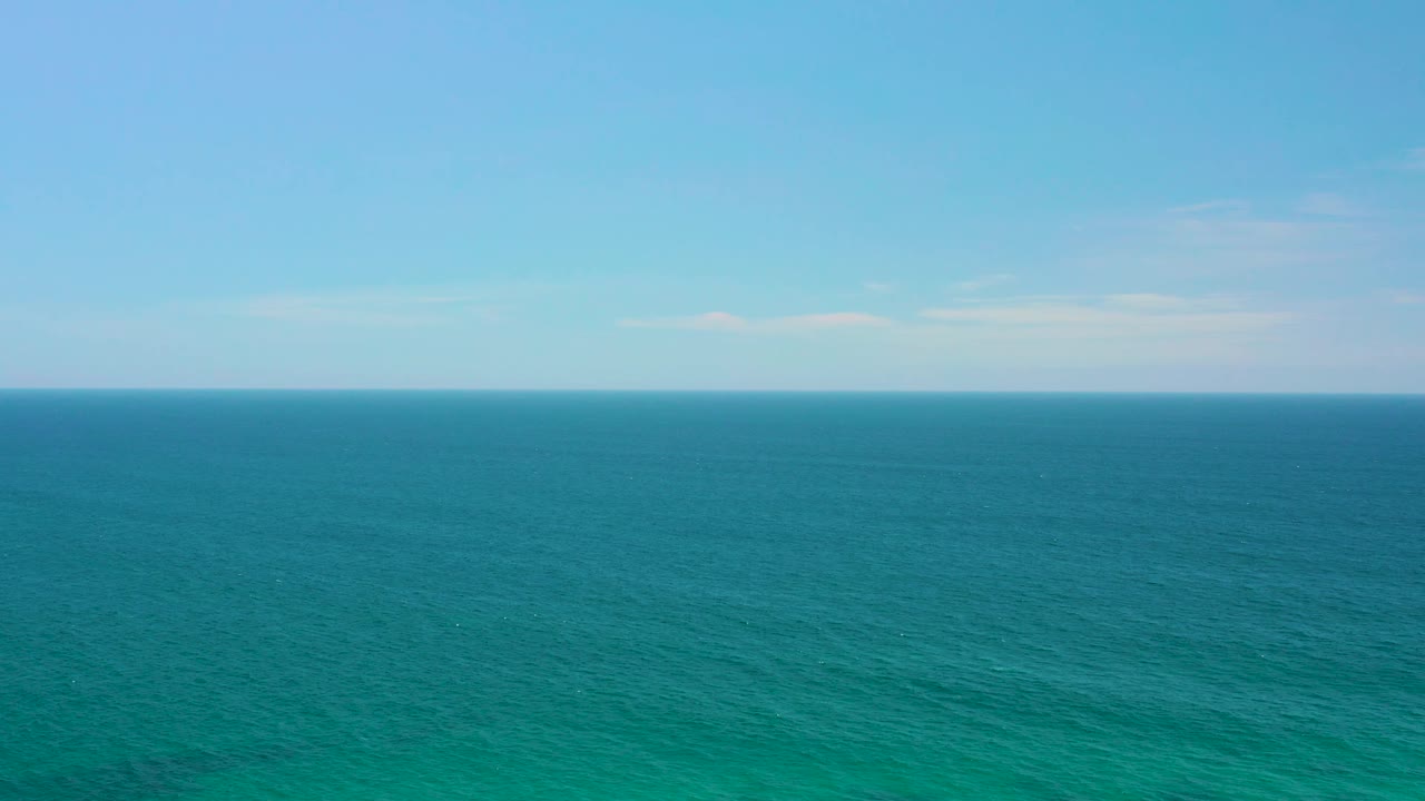 Wide view across clear blue-green water off Shipwrecks Beach, Baja California Sur, with faint ripples in the foreground, pale cloud streaks, and no visible people.