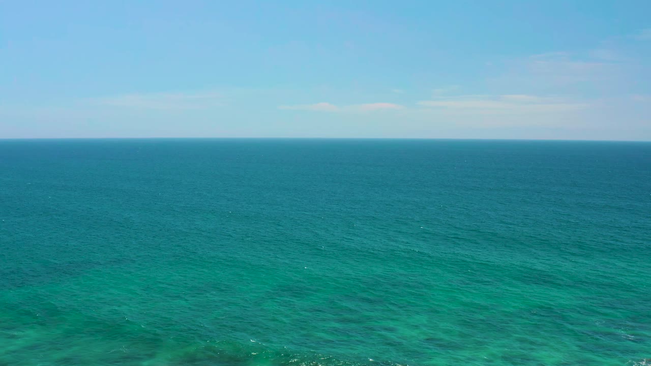 Shipwrecks Beach ocean view with a wide band of blue green water, faint surface texture, pale sky, and no visible people or boats.