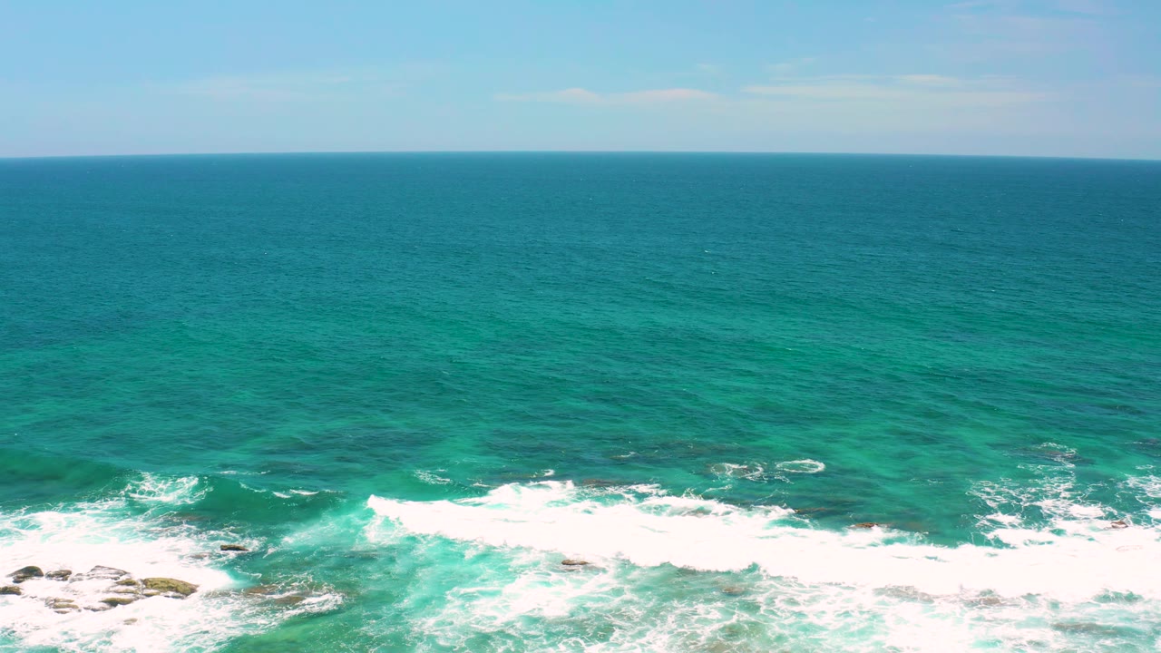 A foamy wave line spreads across shallow rocks below teal water at Shipwrecks Beach, Baja California Sur, with no visible people or structures.