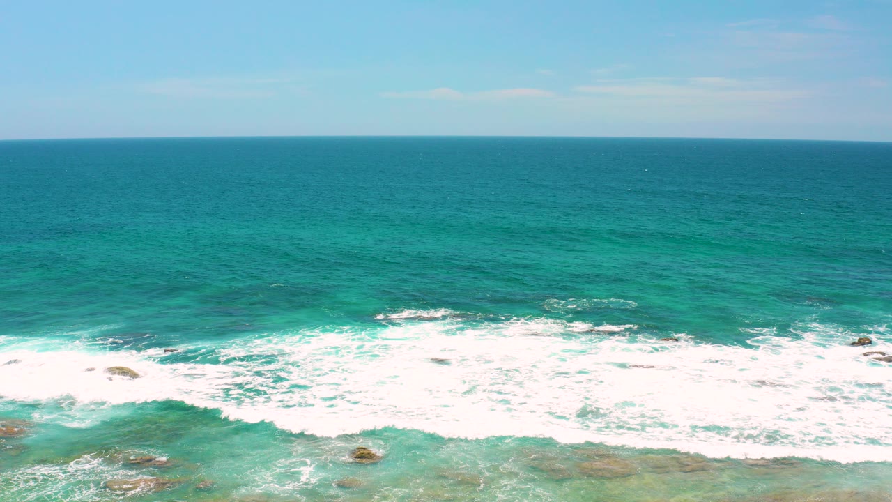 Opening view of Shipwrecks Beach in Baja California Sur, with turquoise water, white surf over low rocks, a bright blue sky, and no visible people.