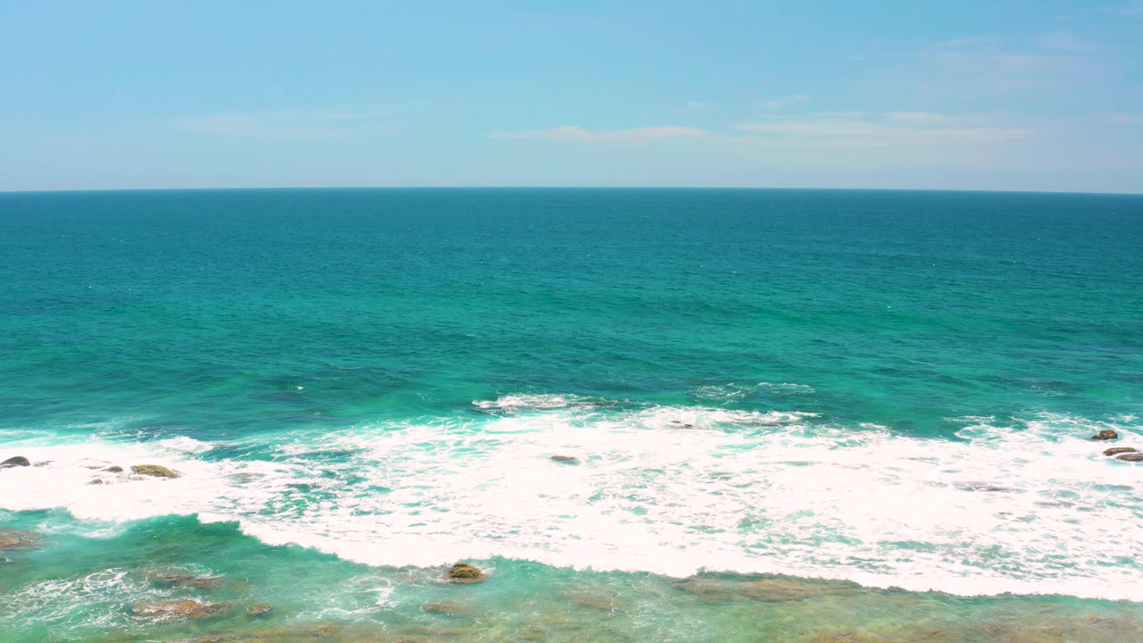Shipwrecks Beach surf rolls in a broad white band toward scattered rocks, with darker teal water beyond the break and no visible people.